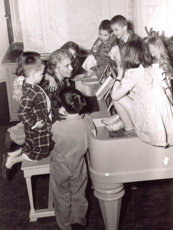 group of children gathered around a woman playing piano